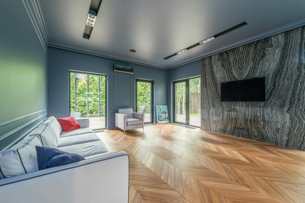 Spacious living room with marble wall, chevron wooden flooring, and ample natural light.